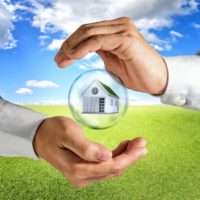 hands enclosing a house in a bubble above grass field and blue sky background
