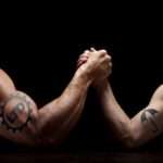 armwrestle-large bicep with 'Ltd' tattooed showing strength over small bicep with a tattoo of an umbrella